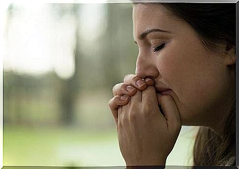 A sad woman holds her hands over her mouth and has her eyes closed.