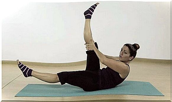 A woman is lying on a yoga mat doing Pilates. 