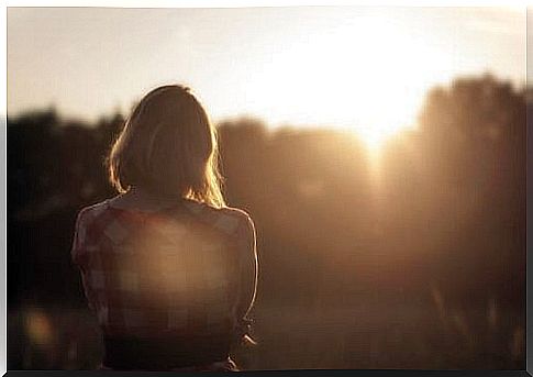 A sad woman looks at the sunset.