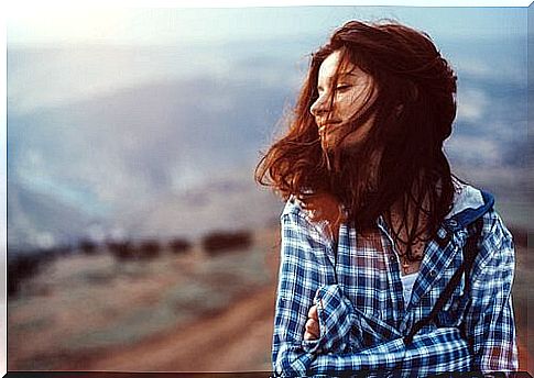 Woman with closed eyes is standing on top of a mountain.