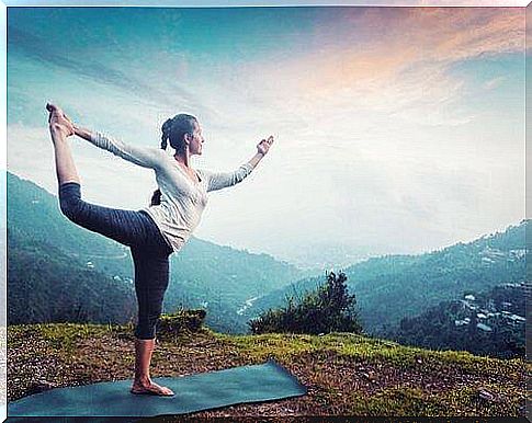 A woman practices yoga on a mat in nature.