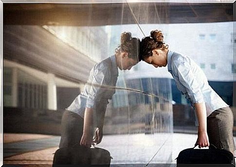 A frustrated woman is standing with her head leaning against a wall.