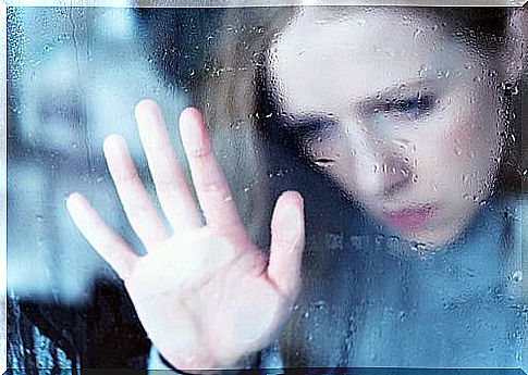 Sad woman puts her hand on window pane