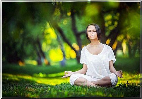 A woman is sitting in the forest and meditating for relaxation.