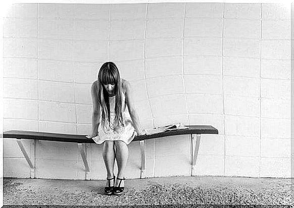 A worried young woman is sitting on a bench. 