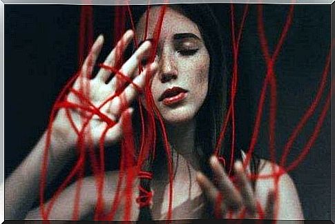 A woman is tied up in a red thread that symbolizes domestic violence and abuse, from which it is difficult to tear ourselves away.