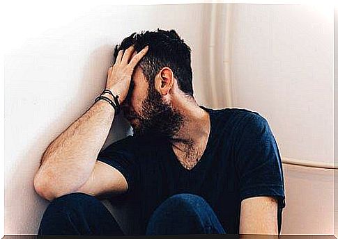 A man suffering from domestic violence and abuse sits huddled on the floor with his hand covering his face.