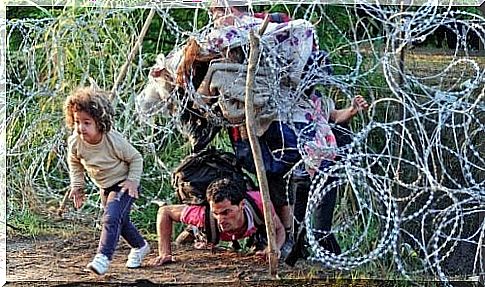 Refugees crawl under a fence