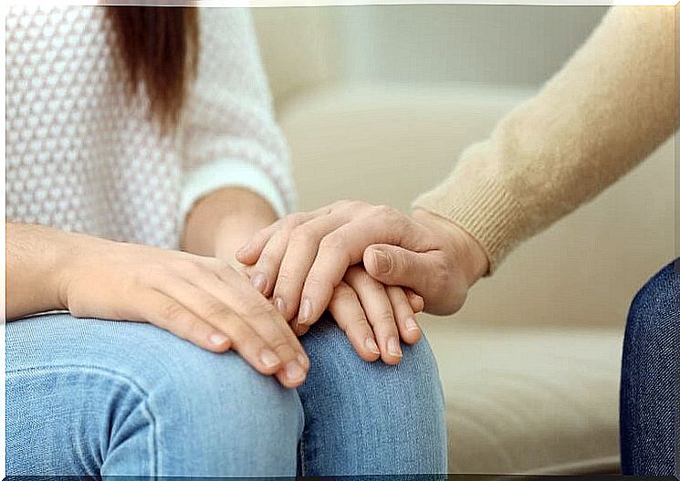 A person is sitting there.  Her hands are on her knees.  Another hand gives consolation.