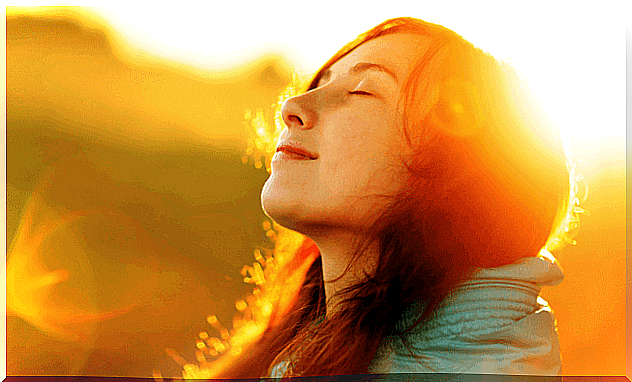 Woman looks up towards the sun with her eyes closed